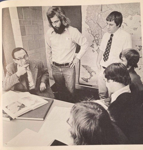 Photo of Classics faculty and students featured in a booklet called “Information for Prospective Students ’76/’77”. Bob Gold seated on the left; Mike Bellhouse, a student of the department and the son of the then-Registrar, centre; and Iain McDougall standing on the right. 