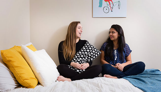 Two students sitting on a bed in a room in residence