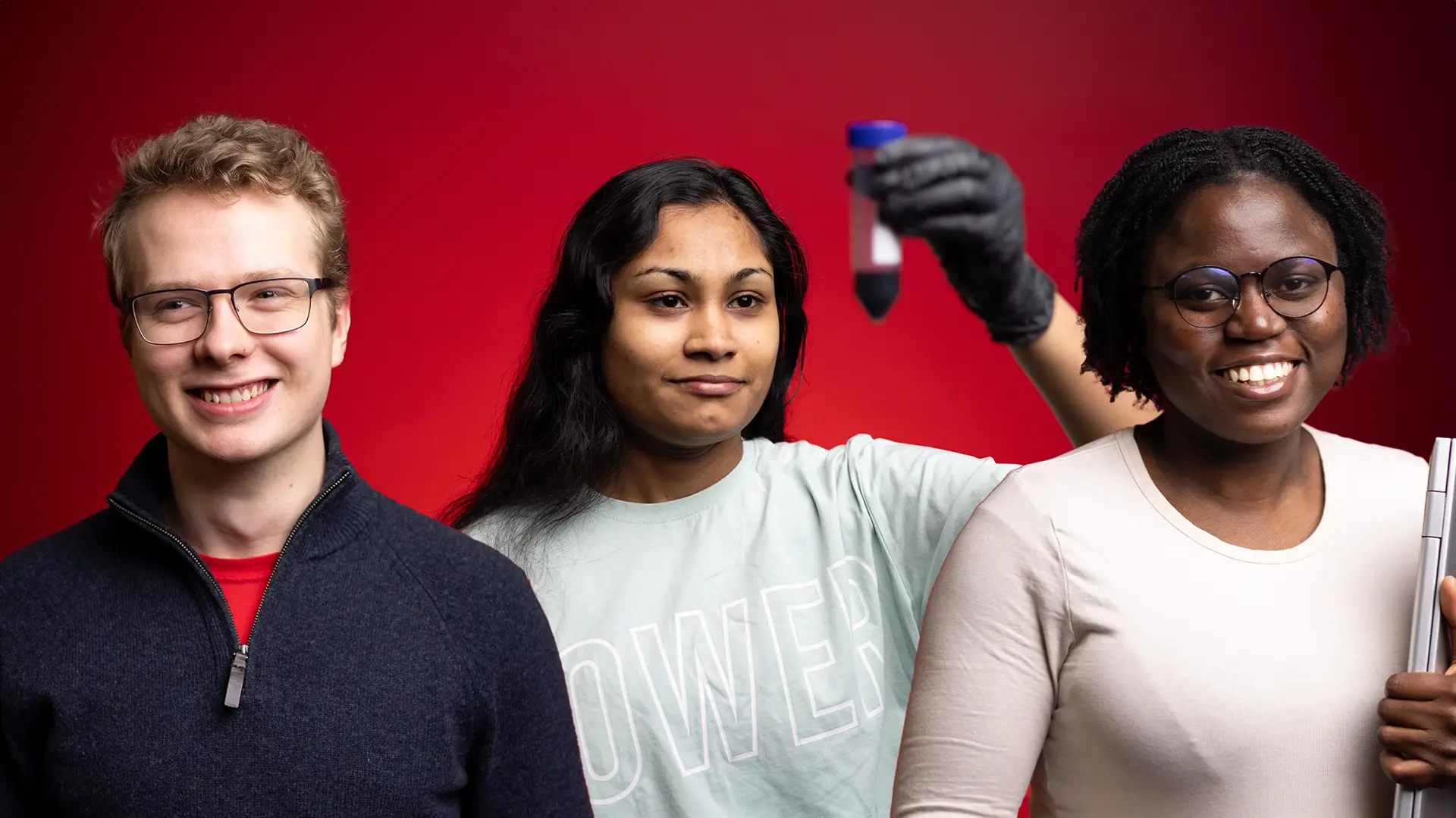 Three students facing camera, one is looking at a test tube, one is holding a laptop