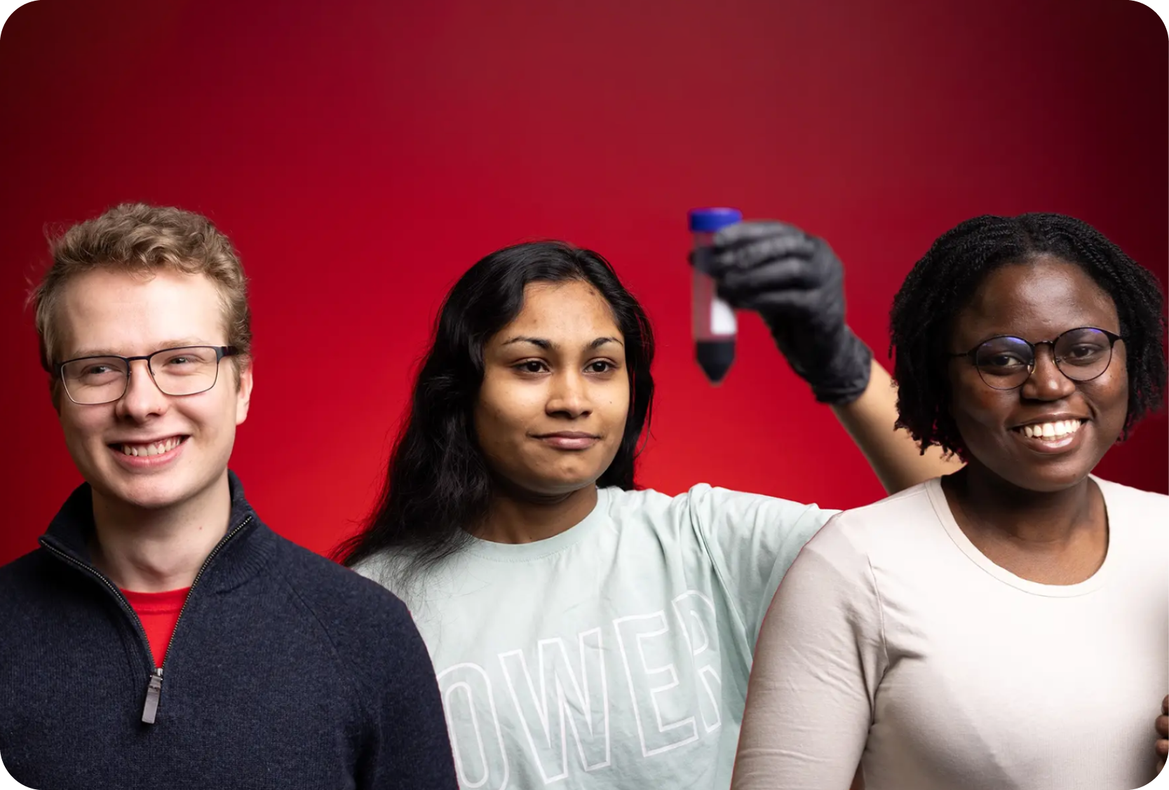 Three students competing in Three-Minute Thesis in front of a red background