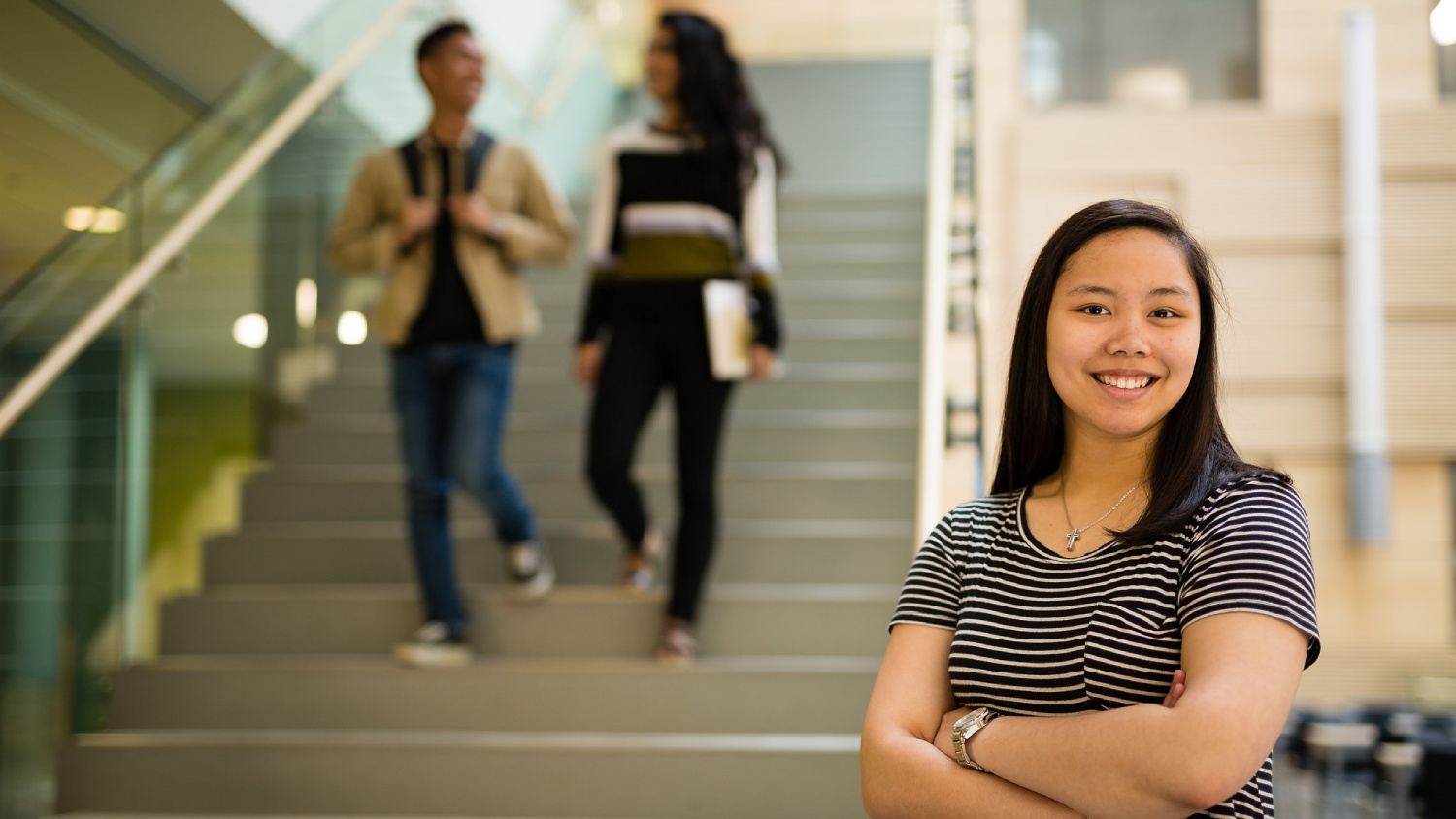 A smiling student standing in front of a staircase