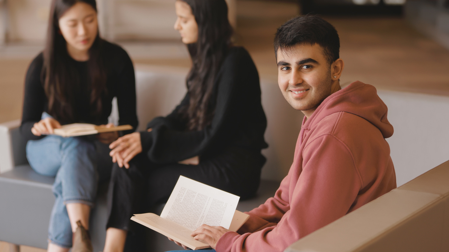 male student with open book, two other female students behind him