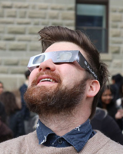 Evan McDonough wearing protective glasses and looking into the sky, presumably to see the 2024 solar eclipse. Wesley Hall appears to be in the background.