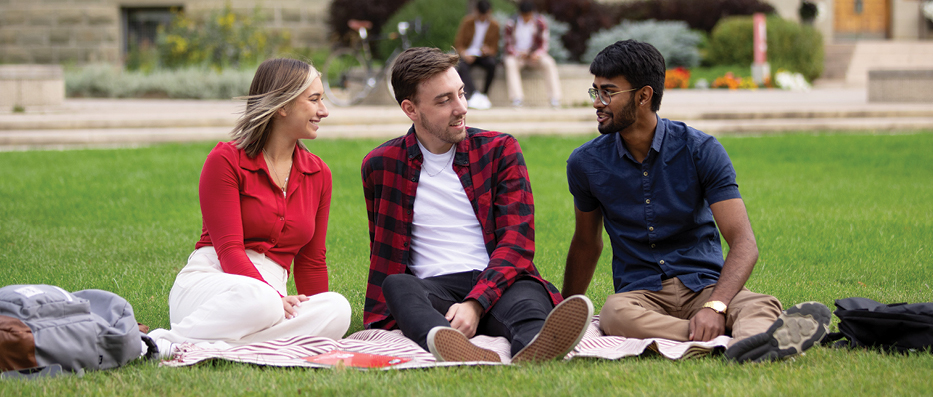 Three students sitting on front lawn of campus