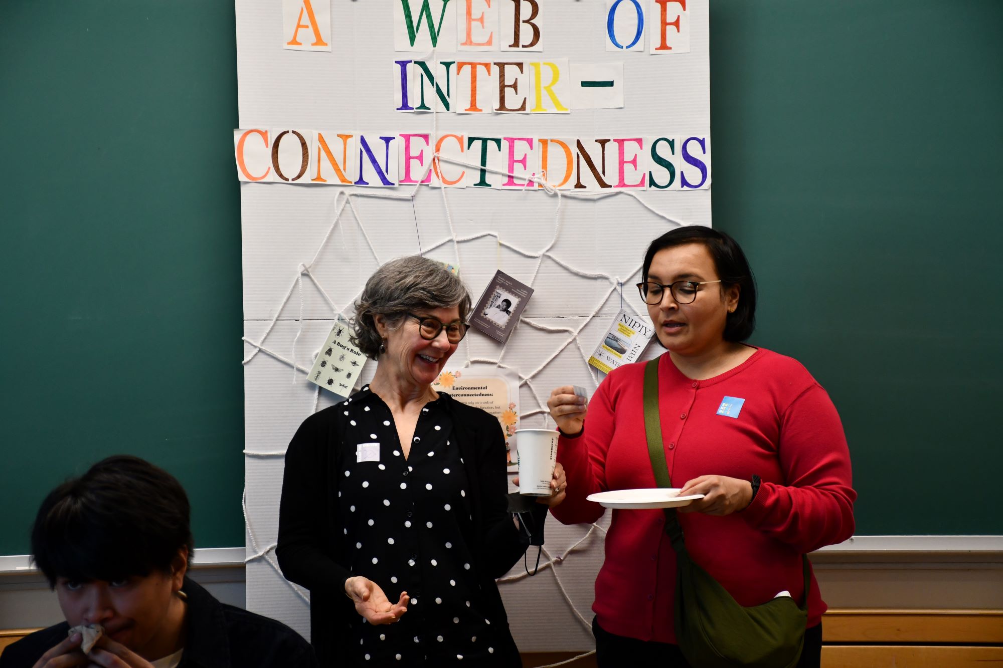 Dr. Fiona Green and Dr. Sharanpal Ruprai announce prize winners while standing in front of the creative contribution, the Web of Interconnectedness, from Dr. Crowe's class