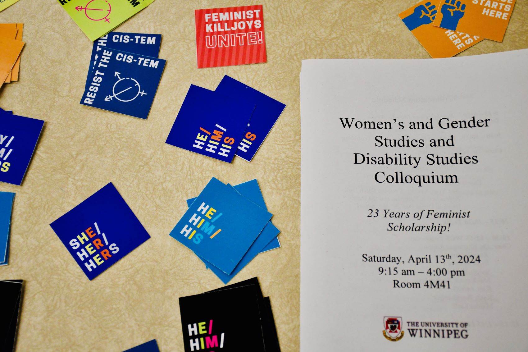 Colloquium program, surrounded by feminist/pronoun stickers